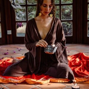 A woman sitting indoors, performing tarot readings with candles and a dreamcatcher.