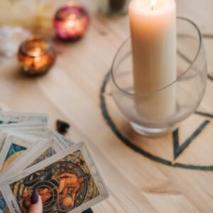 From above of crop anonymous fortune teller with set of tarot cards near burning candles during divination process